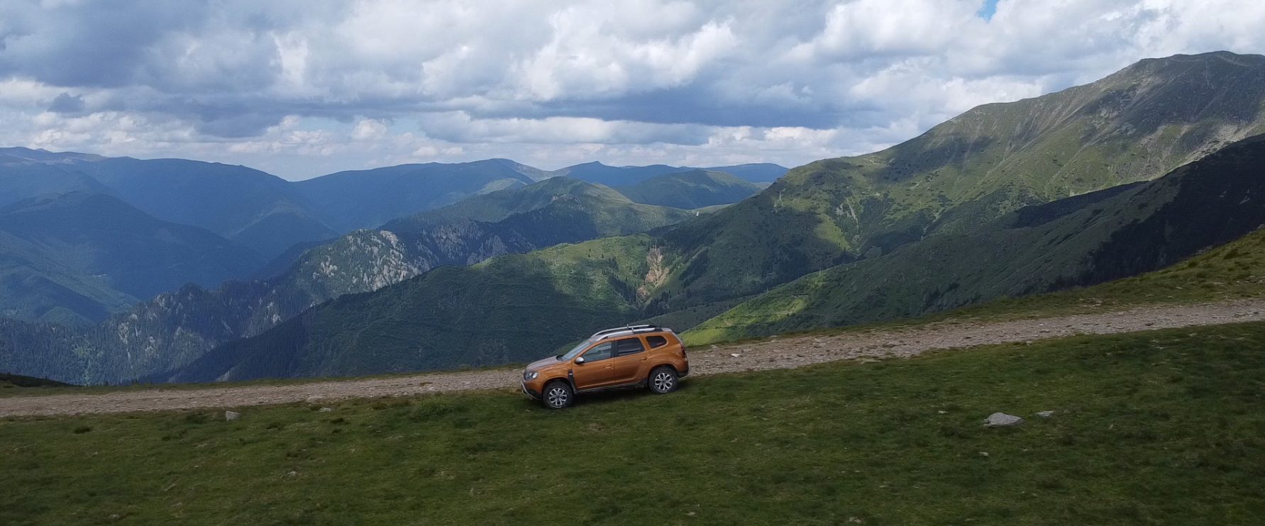 Ridge road high in the Carpathians, with a car small against wide mountain valleys